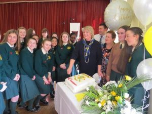 Chairperson of the school's board of management, Nuala Manion cuts the celebration cake surrounded by students.